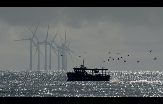 Bateau de pêche devant des éoliennes en mer